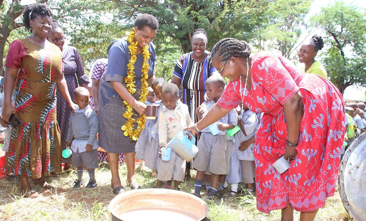 A teacher serves ECDE pupils and Deputy Governor Christine Kilalo porridge during the launch of ECDE feeding program at Taveta on March 13