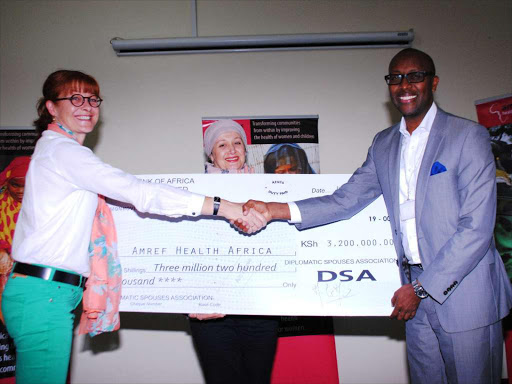 Amref Health Africa Group CEO Githinji Gitahi shakes hands with Marie Celine Marechaux after receiving a cheque as Diplomatic Spouses Association Chair Nabila Maandi looks on