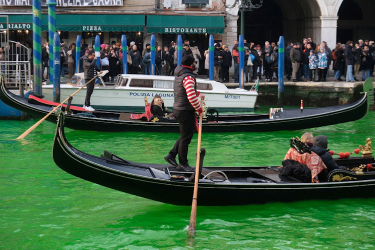 People ride in boats as waters of Grand Canal turned green after a protest by 'Extinction Rebellion' climate activists in Venice, Italy, December 9, 2023.