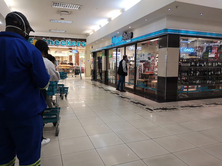 A queue forms outside Checkers Liquor in Northcliff corner, where a customer is seen leaning towards the glass doors to read the alcohol restriction instructions per customer.