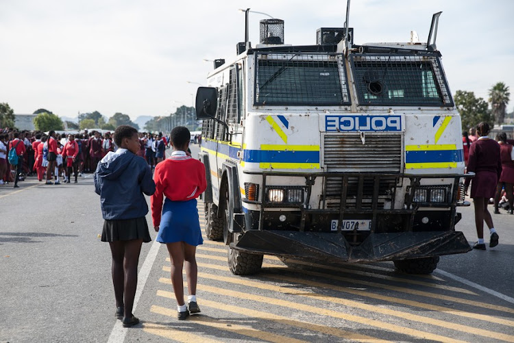 Pupils walk past a police Nyala on Thursday May 16 as protests over school overcrowding hit Kraaifontein, Cape Town, this week.