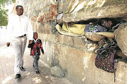 Circa: February, 2017. TUCKED IN: Sean and Bonkosi Mbambo walk past  Mayenzeke   Shiyani , 45, who shelters with his few possessions in a crevice in a decaying wall next to the
Johannesburg Central police station in Commissioner Street, Johannesburg. Pic: Sandile Ndlovu. © The Times.