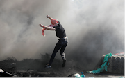 A Palestinian jumps next to a barricade made with tires during an anti-Israel protest over a cross-border violence between Palestinian militants in Gaza and the Israeli military, near Hawara checkpoint near Nablus in the Israeli-occupied West Bank, on May 18 2021. 
