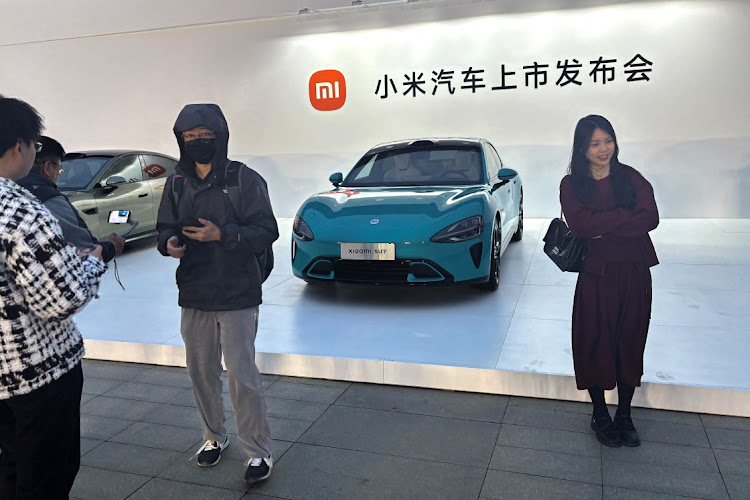 People pose for pictures in front of Xiaomi's first electric vehicle SU7 that is displayed outside the avenue for the car's launch event in Beijing, China March 28, 2024. REUTERS/SARAH WU