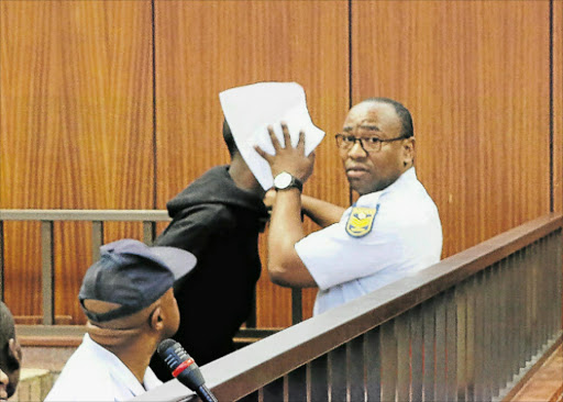 COVER UP: A court guard, Sergeant Chuma Ngaka, shields the face of a suspect charged in the murder of a 59-year-old woman from being photographed by the Daily Dispatch Picture: MALIBONGWE DAYIMANI