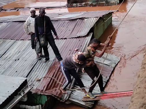 A man holds onto an electricity cable as he is helped get off a rooftop following heavy flooding in parts of Nairobi, April 24, 2024.