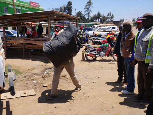 DCI officers collects the bag that caused tension at Nyambare trading center along the Nairobi Nakuru highway on Friday, as boda boda operators watch.