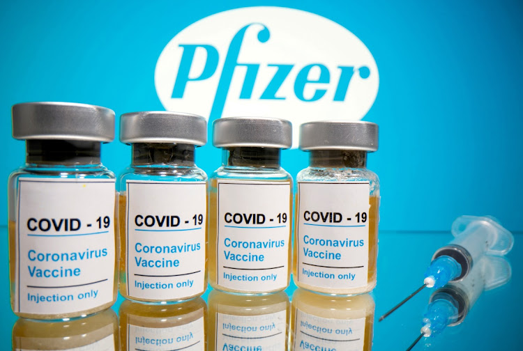Vials with a sticker reading, "Covid-19 / Coronavirus vaccine / Injection only" and a medical syringe are seen in front of a displayed Pfizer logo in this illustration.