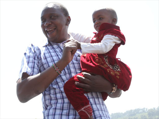 President Uhuru Kenyatta carrries a child during a voter registration drive in Meru on Saturday/ PSCU