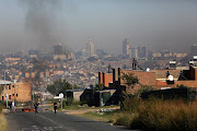 APRIL 25, 2018. People walk on the road  in Alexandra, Johannesburg. A barricaded road forms the backdrop.