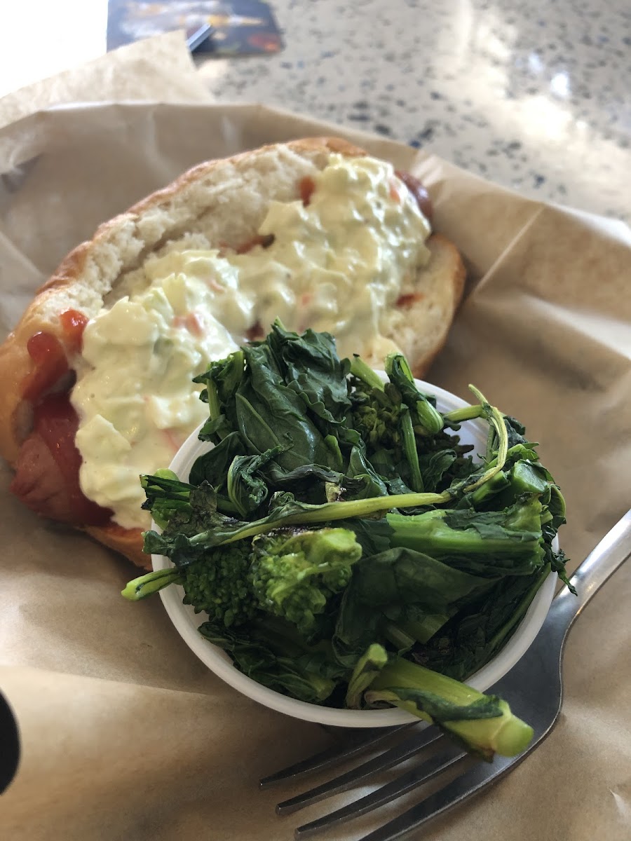 Gluten free hot dog with ketchup and coleslaw. One of the gluten free sides is broccoli rabe.