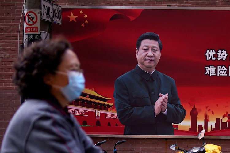 FILE PHOTO: A woman wearing a protective mask is seen past a portrait of Chinese President Xi Jinping on a street as the country is hit by an outbreak of the coronavirus, in Shanghai, China March 12, 2020. REUTERS/Aly Song