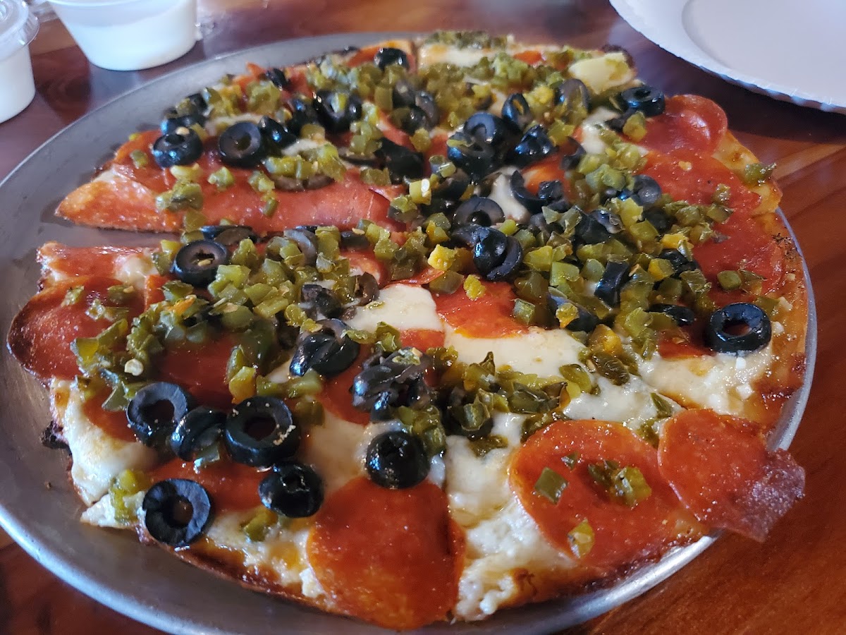Small pepperoni, olive, and jalapeno pizza with garlic sauce on gluten free crust