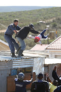 A Nelson Mandela Bay metro police officer grabs the father as he throws his child off the roof of a shack at the Joe Slovo informal settlement in Port Elizabeth on 12 April 2018.