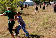 A bloody female zombie chases a runner as a horde of other zombies stand waiting for more runners to come by in the 2013 Run For Your Lives 5K event in the USA.