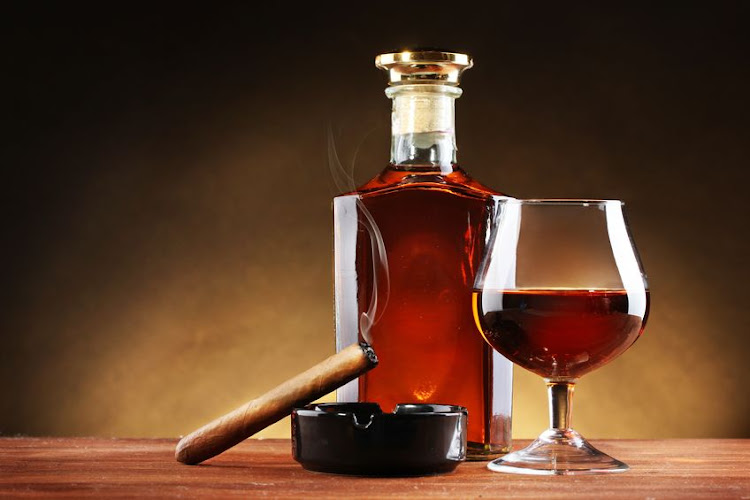 Bottle and glass of brandy and cigar on wooden table on brown background