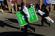 A man carries political party posters while voters wait their turn in Alexandra, Johannesburg. 