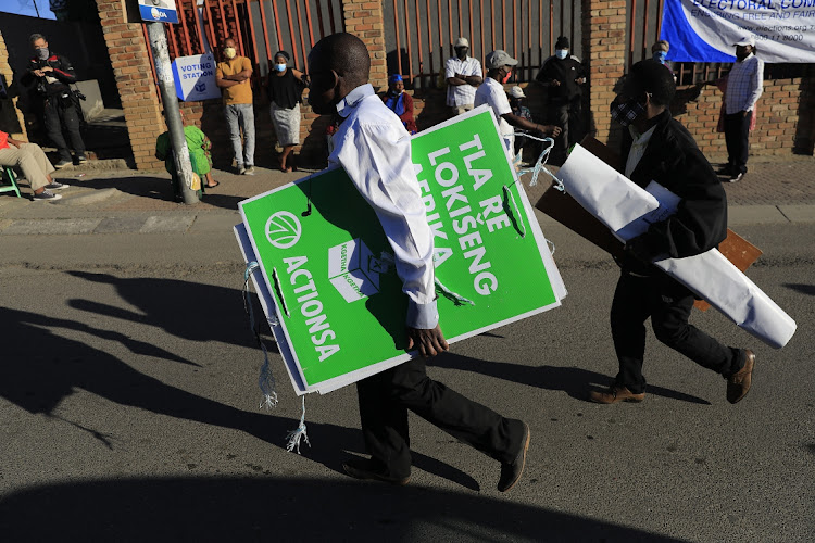A man carries political party posters while voters wait their turn in Alexandra, Johannesburg.