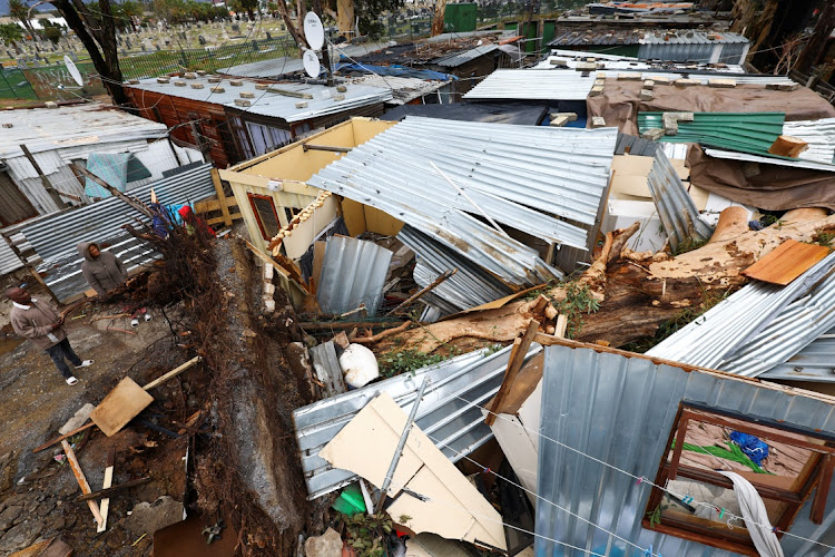 People look at a house in an informal settlement after it was destroyed by a tree during severe wind in Somerset West.