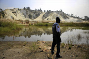 SCENE OF DEATH: A policeman looks at a mine dump near the scene where eight illegal miners were found dead in Benoni, east of Johannesburg, on Monday. It is suspected that the miners were killed by rival illegal mining gangs.