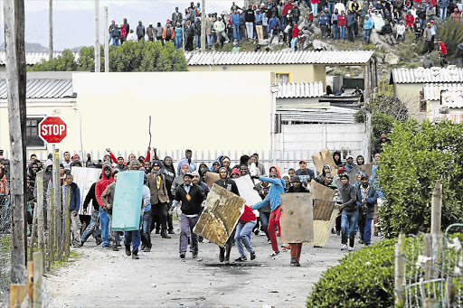 AT THE GATE: Protesters throw stones and taunt police on a third consecutive day of rioting in Grabouw yesterday. Police closed the N2 highway near Sir Lowry's Pass and fired teargas and water cannon to disperse the crowds