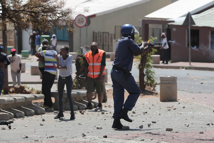 A police officer fires rubber bullets while being pelted by rocks by protesters in Westbury, Johannesburg, on October 1 2018.