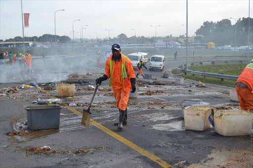 Sanicare workers clean a road full of human feces left by protesters in Cape Town, South Africa. Sannicare janitors responsible for cleaning communal toilets blocked a portion of the N2 highway with burning tyres last week and dumped faeces on the road, in protest against being dismissed.