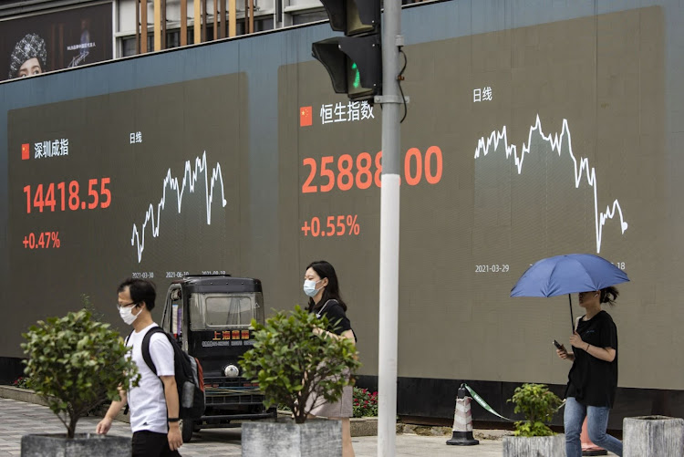 Pedestrians walk past a public screen displaying the Shenzhen Stock Exchange and the Hang Seng Index figures in Shanghai, China. Picture: BLOOMBERG/QILAI SHEN