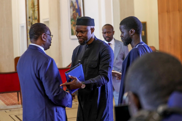 Senegal's new leader Bassirou Diomaye Faye stands while Ousmane Sonko shakes hands with outgoing President Macky Sall at the presidential palace in Dakar, March 28 2024. Picture: SENEGAL PRESIDENCY/REUTERS