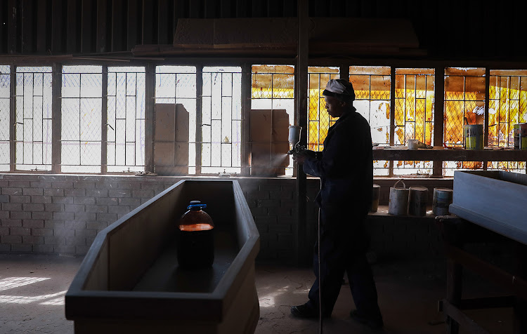 Johannes Mandlathi, a carpenter at Malusi Coffin Manufacturers in Emdeni, Soweto primes a coffin before hand-painting it. The manufacturers say demand for coffins and caskets has gone up due to the number of Covid-19 related deaths.