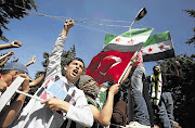 Syrian refugees wave Turkish and Syrian independence flags during a protest against President Bashar al-Assad at Yayladagi refugee camp in Hatay province, Turkey, just across the border from Syria Picture: UMIT BEKTAS/REUTERS