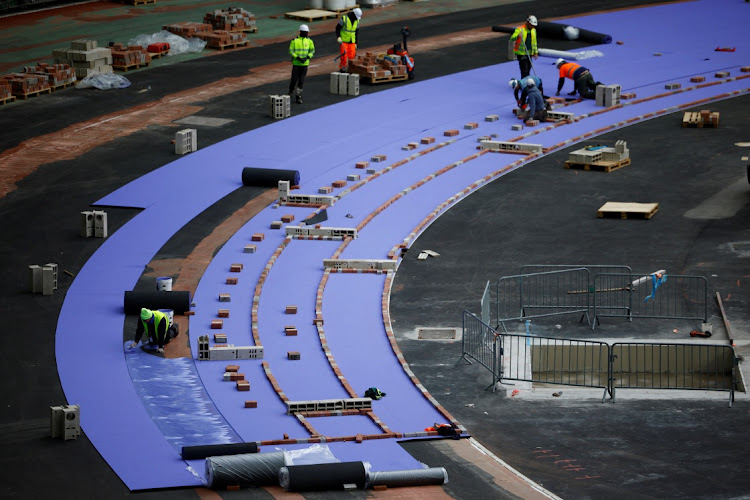 Workers install the Paris 2024 Olympic and Paralympic Games' athletics track of two shades of purple manufactured by Mondo Sports Flooring inside the Stade de France, in Saint-Denis near Paris on April 9.
