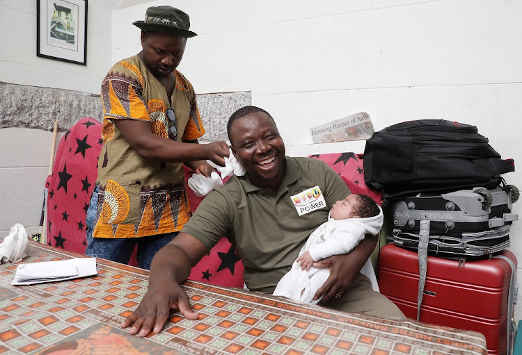 Refugee leader JP Balus holds a child born in the Central Methodist Church while he is patted down with toilet paper by another refugee.