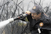 SHOULDER CHARGE: A firefighter hoses down smouldering vegetation near Fish Hoek. What was unusual about this fire wasn't its size, but the fact that the homes it threatened didn't for the most part belong to the poor