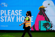 FILE PHOTO: An essential worker walks past a 'Please Stay Home' sign on the first day of a five-day lockdown implemented in the state of Victoria in response to a coronavirus disease outbreak in Melbourne, Australia, on February 13, 2021. 
