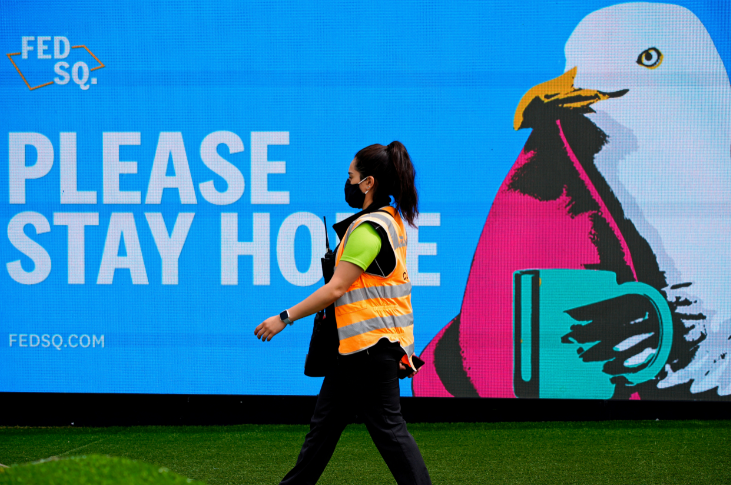 FILE PHOTO: An essential worker walks past a 'Please Stay Home' sign on the first day of a five-day lockdown implemented in the state of Victoria in response to a coronavirus disease outbreak in Melbourne, Australia, on February 13, 2021.