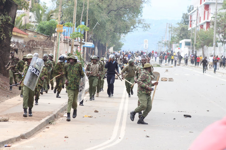 Police officers take cover as Azimio supporters run after them along Kisumu-Busia road. PHOTO/DANIEL OGENDO