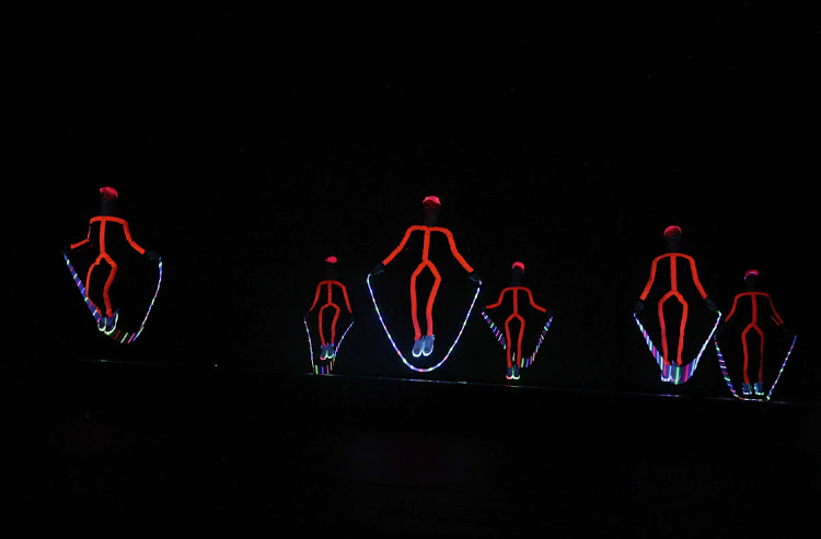 Dancers wearing neon glowing suits create an artistic dance, setting the stage on fire.