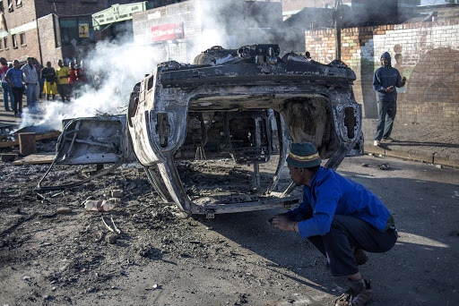 RUNNING AMOK: People look at a burnt-out car purportedly torched in the early hours of yesterday morning outside the Jeppe Hostels in Johannesburg Picture: AFP