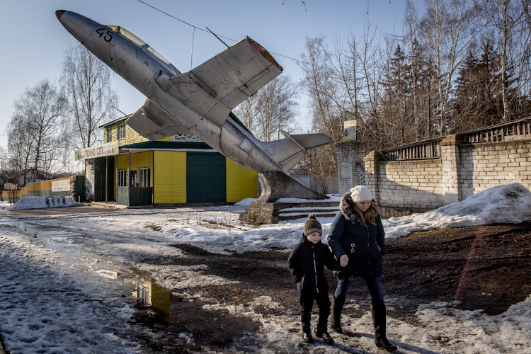 A woman walks underneath a military plane set as a monument to a former military base at a town on the outskirts of the Three Sisters border crossing between, Ukraine, Russia and Belarus on February 14, 2022