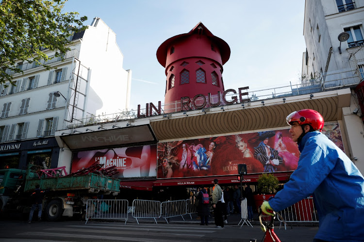A cyclist passes by the Moulin Rouge, Paris' most famous cabaret club, after the sails of the landmark red windmill on its top fell off during the night in Paris, France, on April 25 2024.
