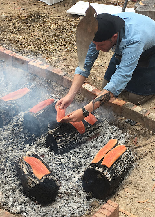 Wesley Randles prepares trout on tree trunks on an open fire