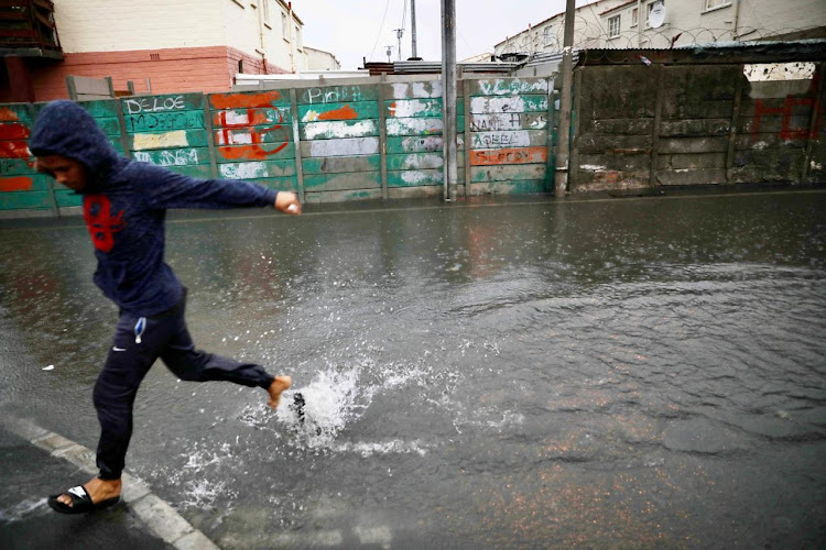 A child skips through a deep puddle on a road in Hanover Park on the Cape Flats.