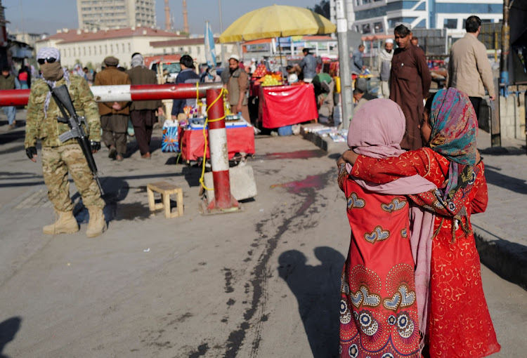 Girls cuddle each other as they walk past a Taliban fighter at a market in Kabul, Afghanistan October 24, 2021.