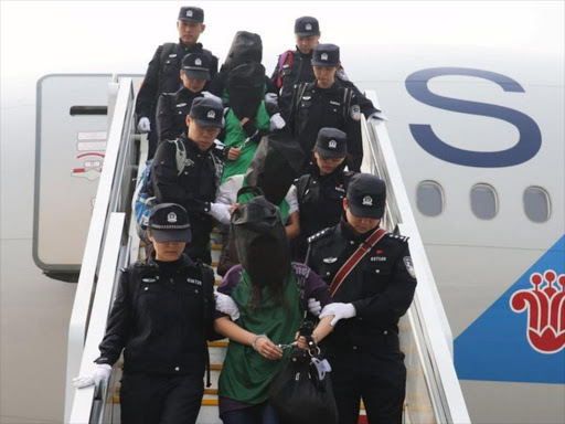 Police escort a group of people wanted for suspected fraud in China, after they were deported from Kenya.PHOTO/REUTERS