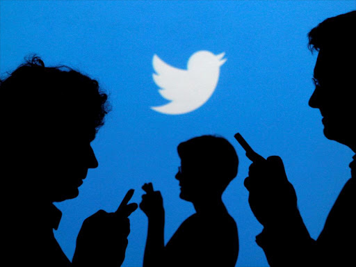 People holding mobile phones are silhouetted against a backdrop projected with the Twitter logo. /REUTERS