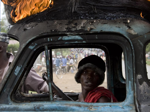 A man sits inside a destroyed vehicle with a burning tyre on its roof during post-election violence in Kisumu on January 29, 2008. \ YASUYOSHI CHIBA /AFP PHOTO