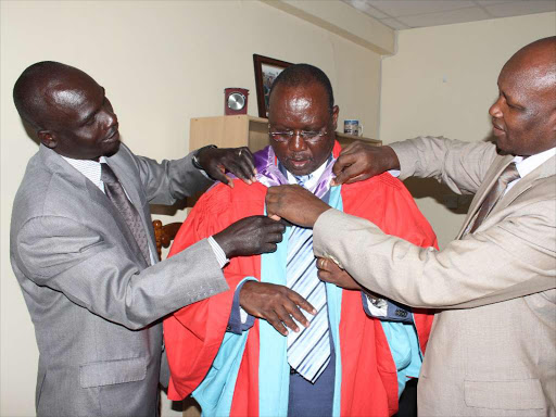 Former Inspector General of Police David Kimaiyo (centre) is assisted in putting a graduation gown last Thursday. He graduated with a PhD in sociology for the University of Nairobi /COLLINS KWEYU