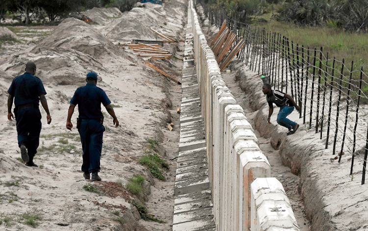 A man crosses into South Africa through the border fence with Mozambique while South African security officials patrol next to the unfinished concrete barrier wall being erected to stop stolen cars being driven across the border. The government intends to restart work on the fence. File image.