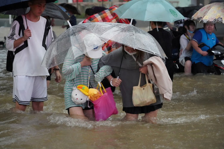 Residents, holding umbrellas amid heavy rainfall, wade through floodwaters on a road in Zhengzhou, Henan province, China, on July 20 2021. Picture: CNSPHOTO VIA REUTERS